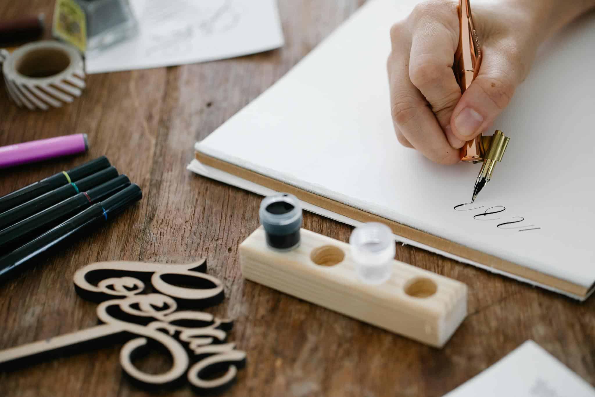 Close-up of hand lettering with a pen and ink on a wooden table, showcasing artistic calligraphy.