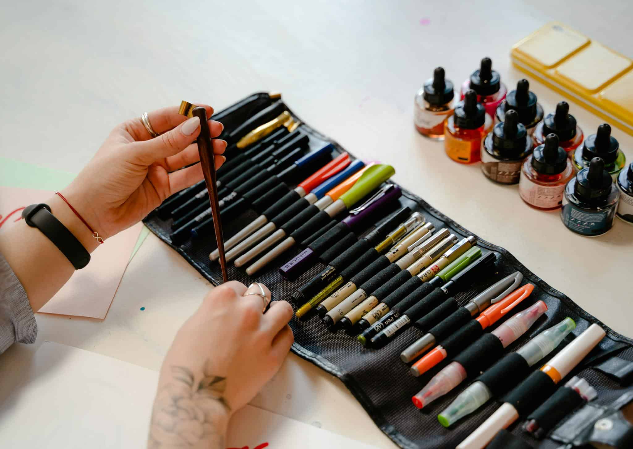 Hands arranging art supplies and ink bottles, perfect for creative projects.